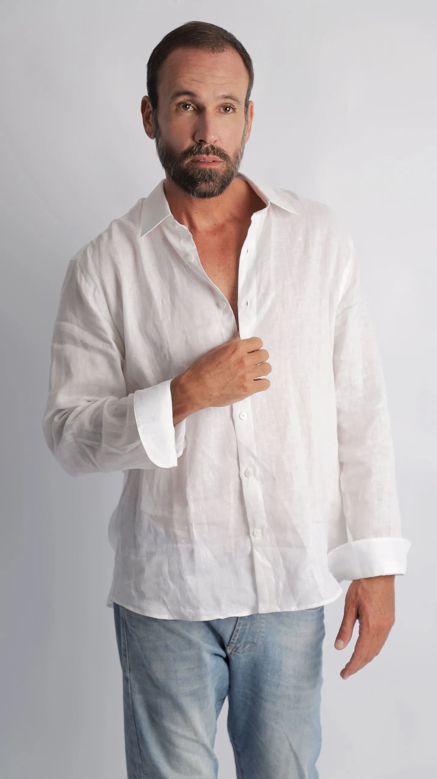 Vini Cavalieri de camisa branca de linho e jeans, em fundo cinza claro