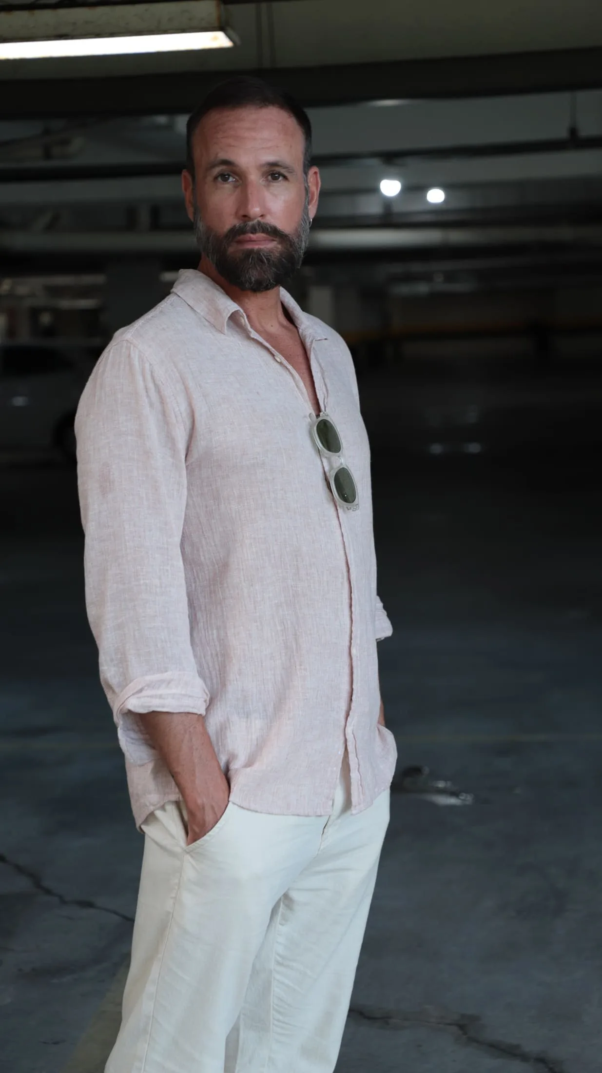Vini Cavalieri de camisa de linho e calça clara, com as mãos nos bolsos numa garagem escura