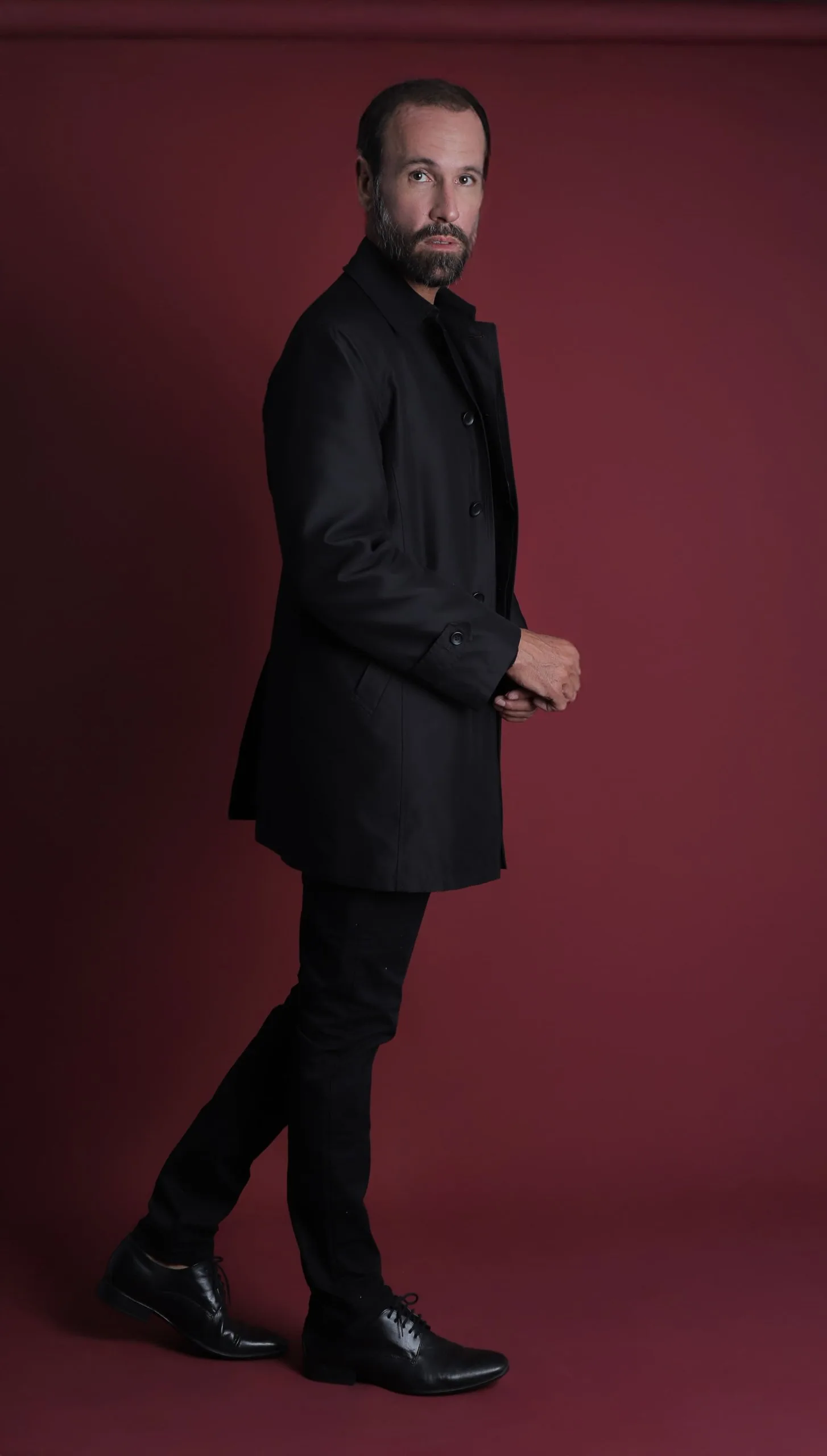 Vini Cavalieri de perfil, de casaco preto, caminhando em fundo vinho