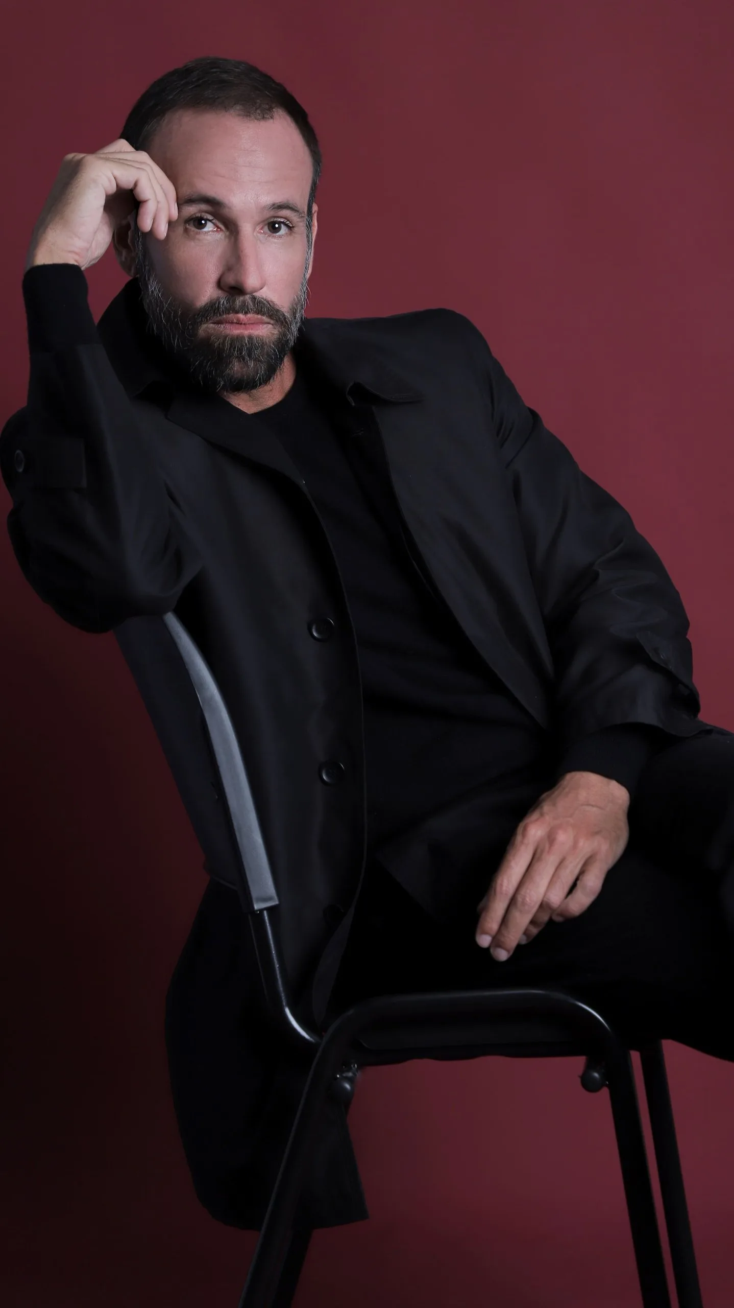 Vini Cavalieri de preto, sentado numa cadeira em fundo vinho