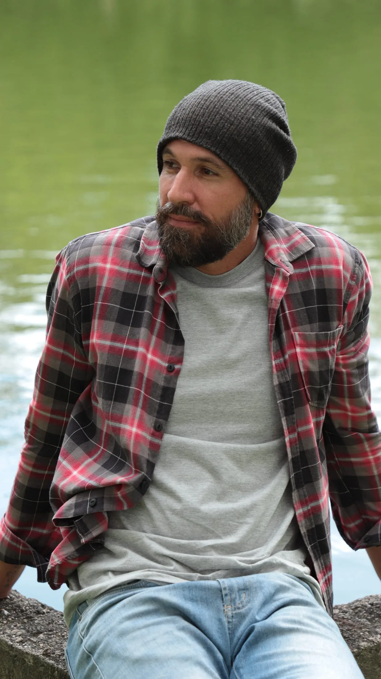 Vini Cavalieri de gorro e camisa xadrez, sentado à beira de um lago