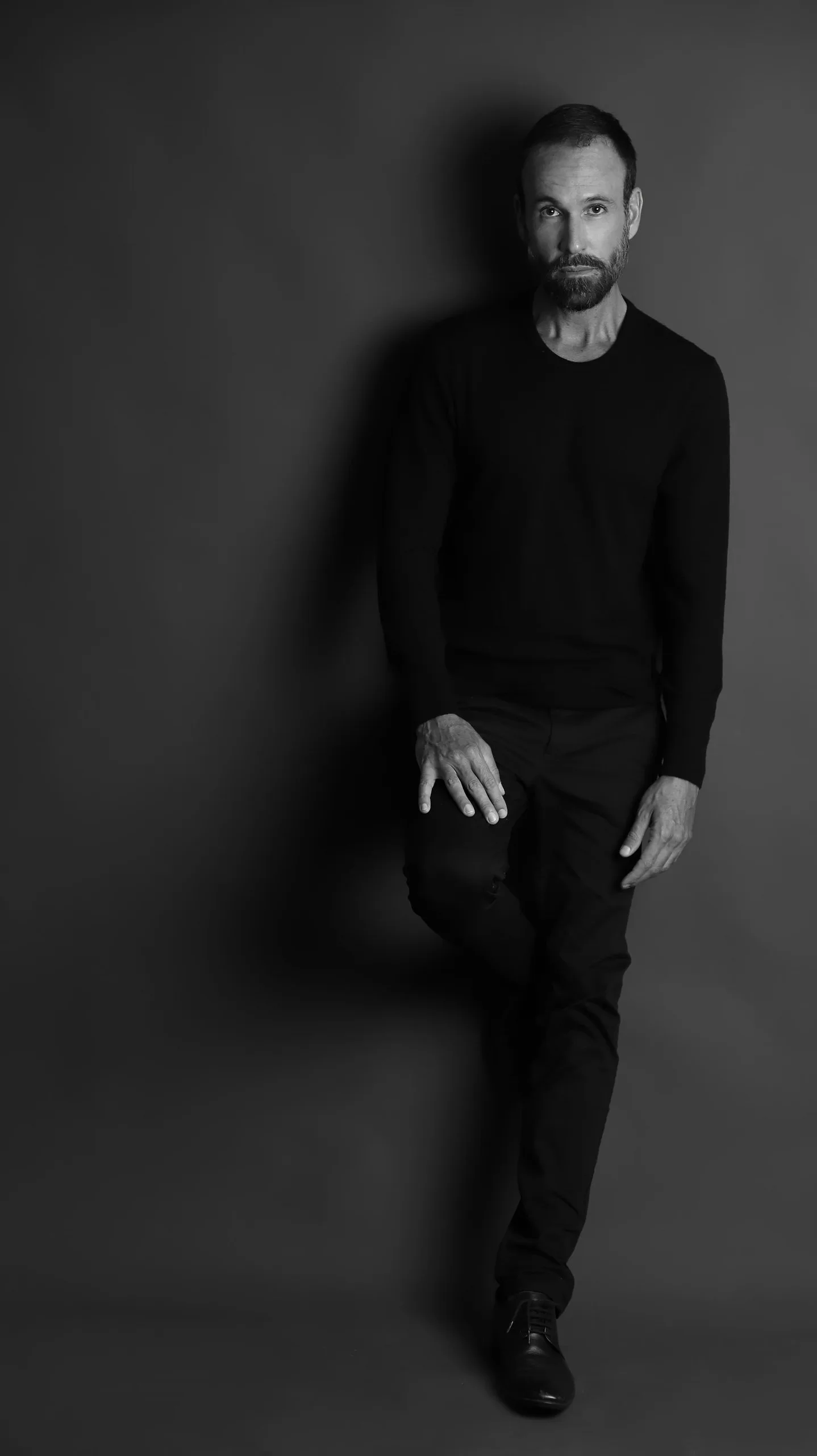 Vini Cavalieri em preto e branco, de corpo inteiro, todo de preto
