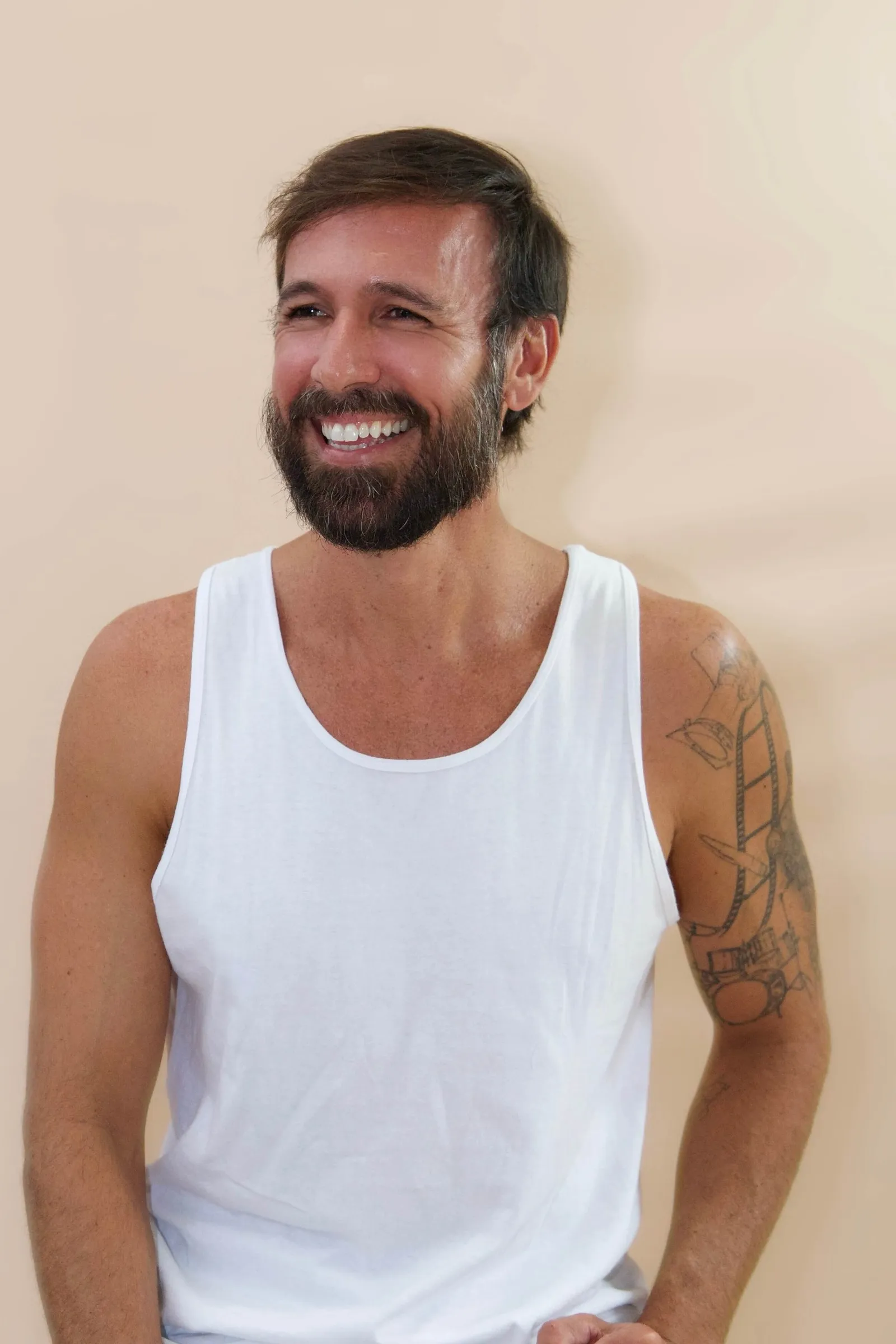 Vini Cavalieri sorrindo, de regata branca, em fundo bege