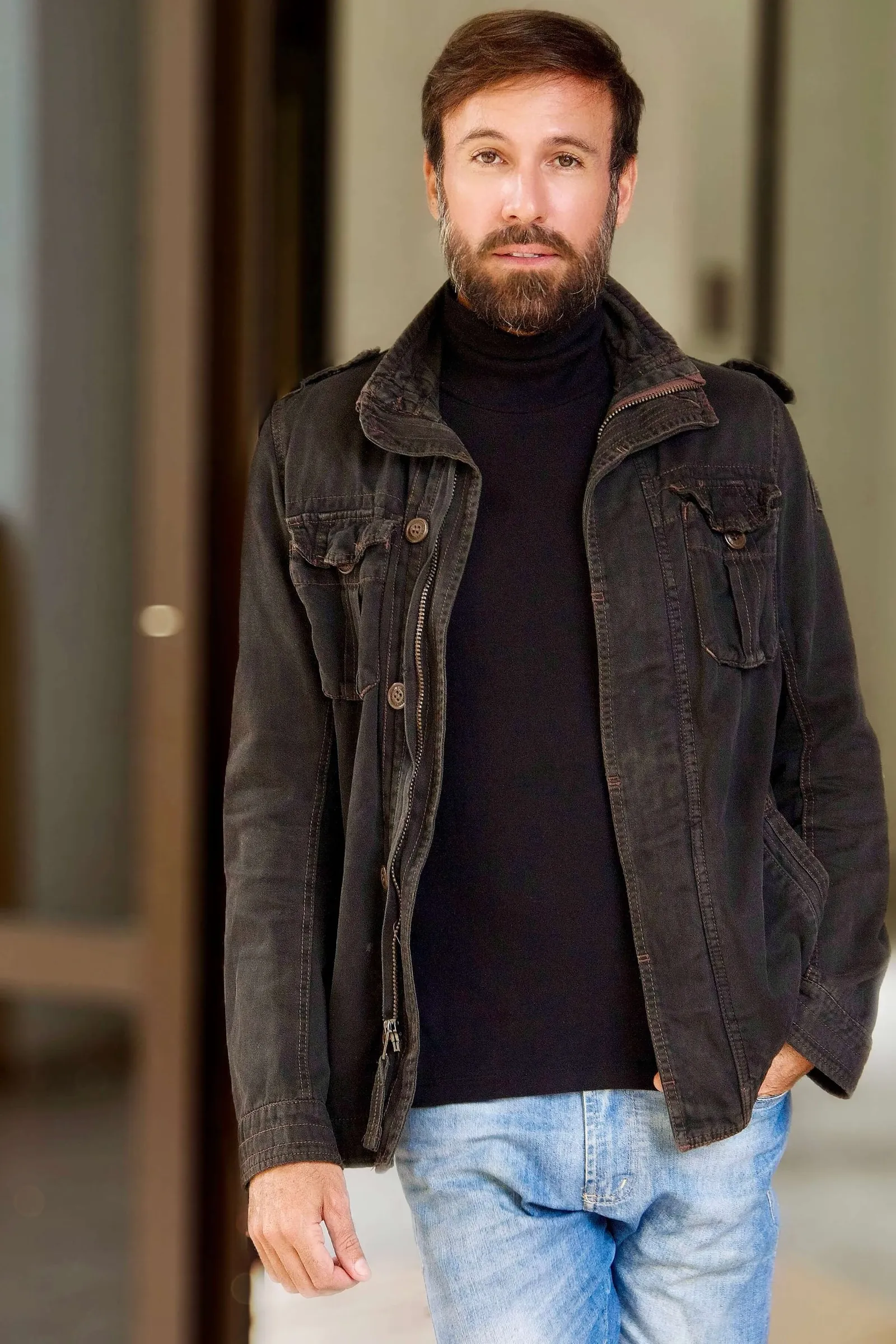 Vini Cavalieri de jaqueta escura, gola alta e jeans, num corredor