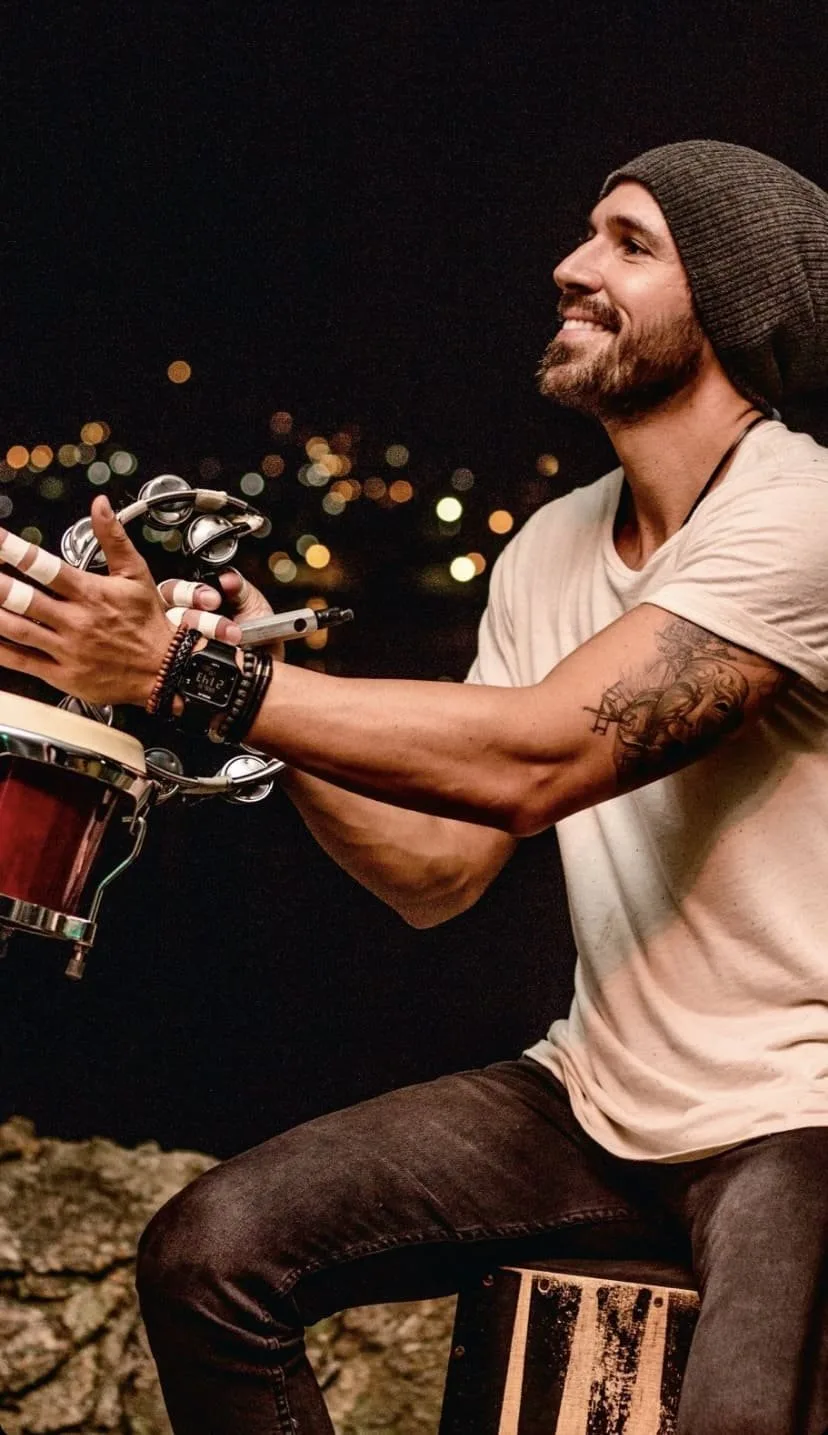Vini Cavalieri de gorro, tocando percussão ao ar livre à noite