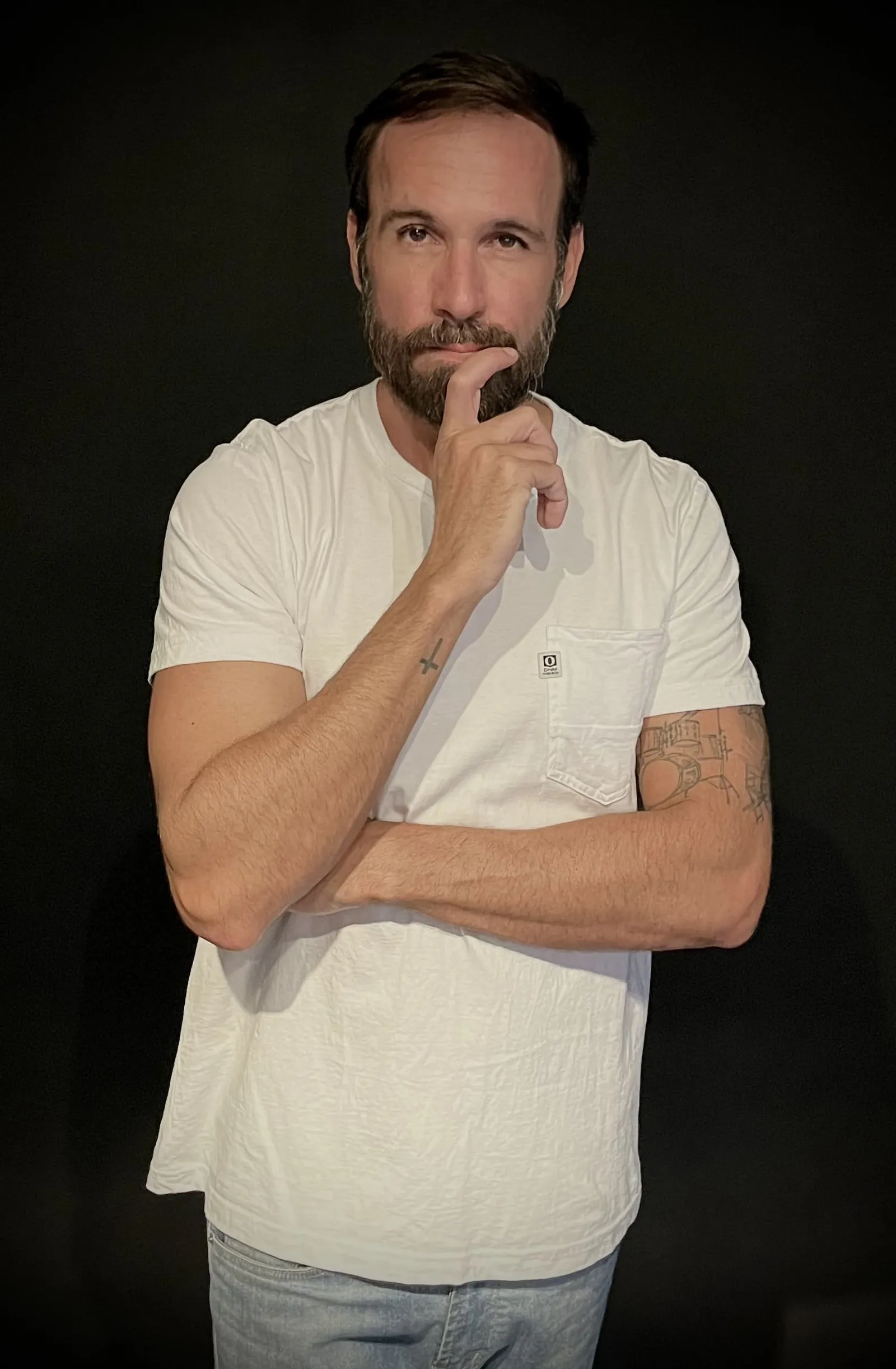 Vini Cavalieri de camiseta branca, com a mão no queixo, em fundo preto