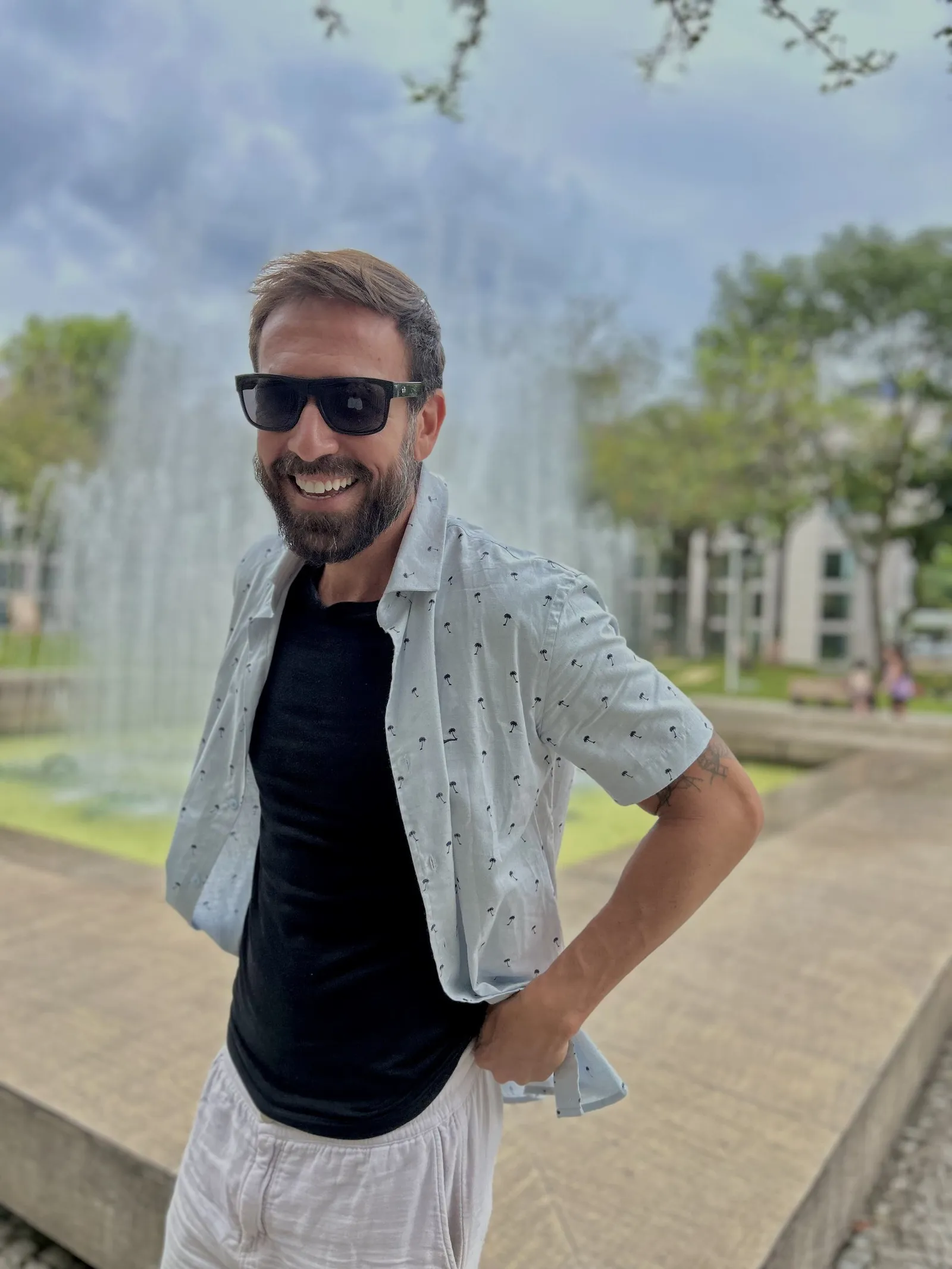 Vini Cavalieri sorrindo, de óculos escuros, junto a uma fonte