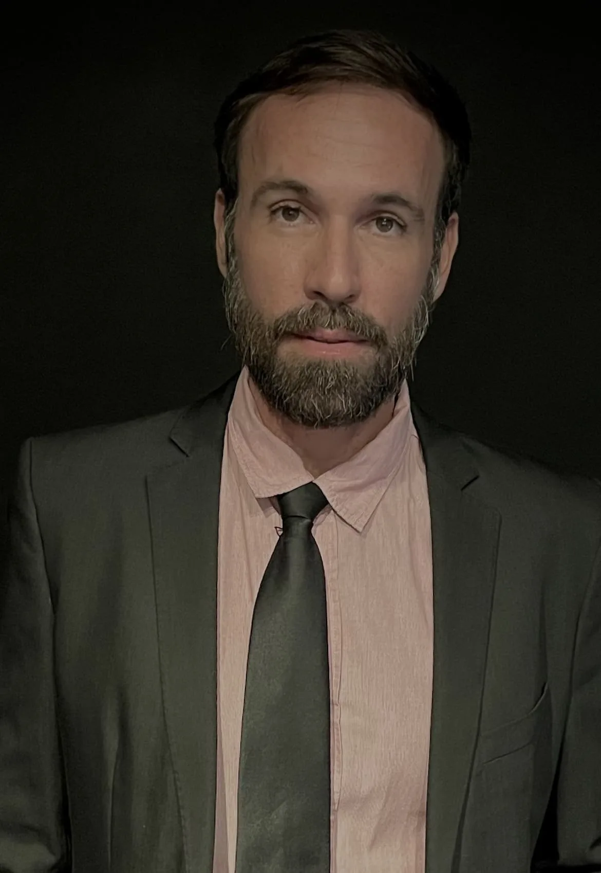 Vini Cavalieri de terno, camisa rosa e gravata, em fundo preto