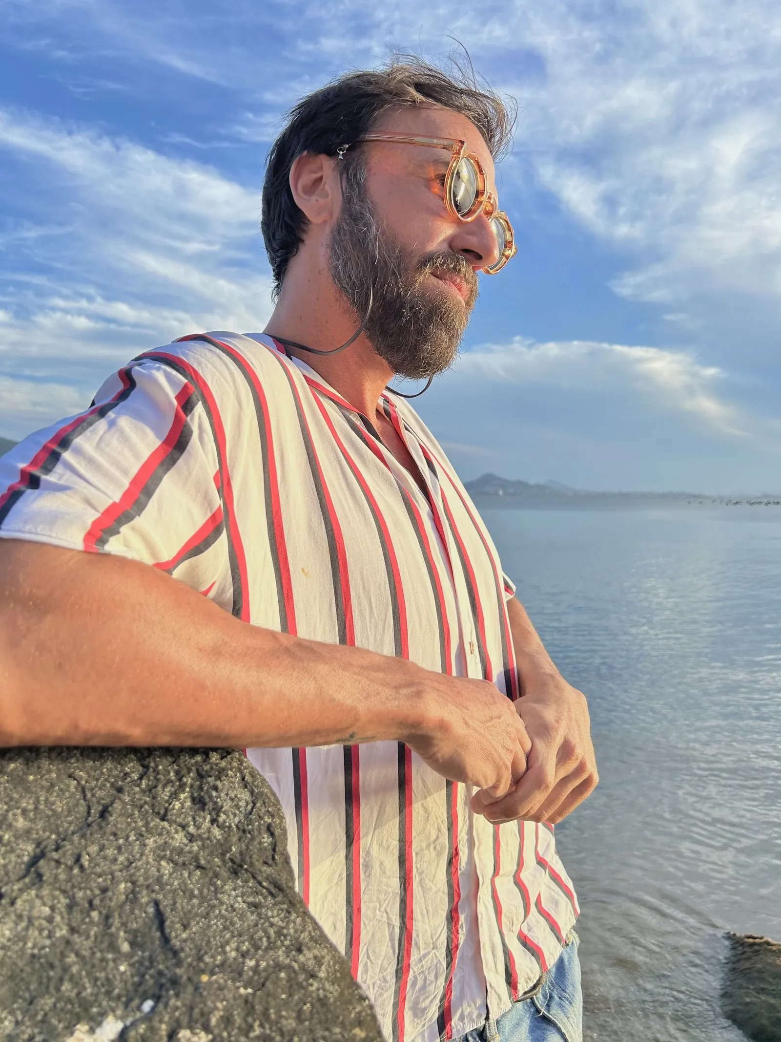 Vini Cavalieri de camisa listrada e óculos, junto ao mar
